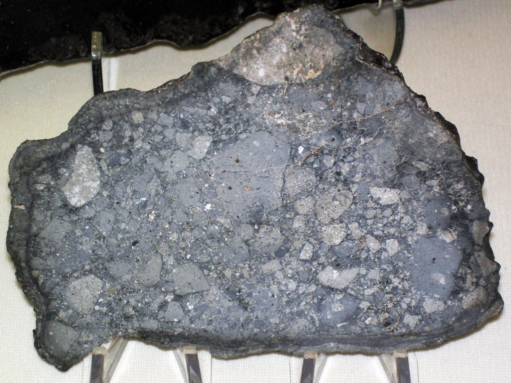 Eukryt NWA 6694 – achondryt będący brekcją bazaltową, reprezentujący materiał pochodzący ze zróżnicowanego ciała planetarnego. Eukryty wiązane są z planetoidą (4) Westa. Fot. James St. John, CC BY 2.0, via Wikimedia Commons