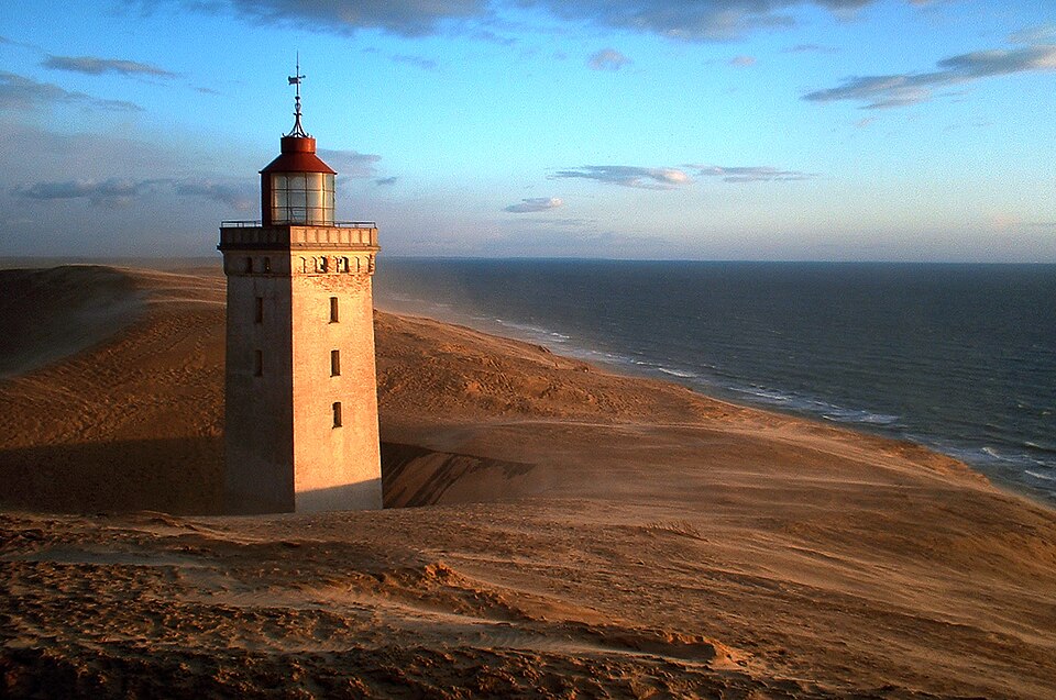 Rubjerg Knude na wybrzeżu Morza Północnego w Danii. Wiatr transportujący piasek oraz postępująca abrazja morska przez dziesięciolecia nieustannie zmieniały krajobraz wokół latarni. Fot. AnneCN, Wikimedia Commons, CC BY 2.0.